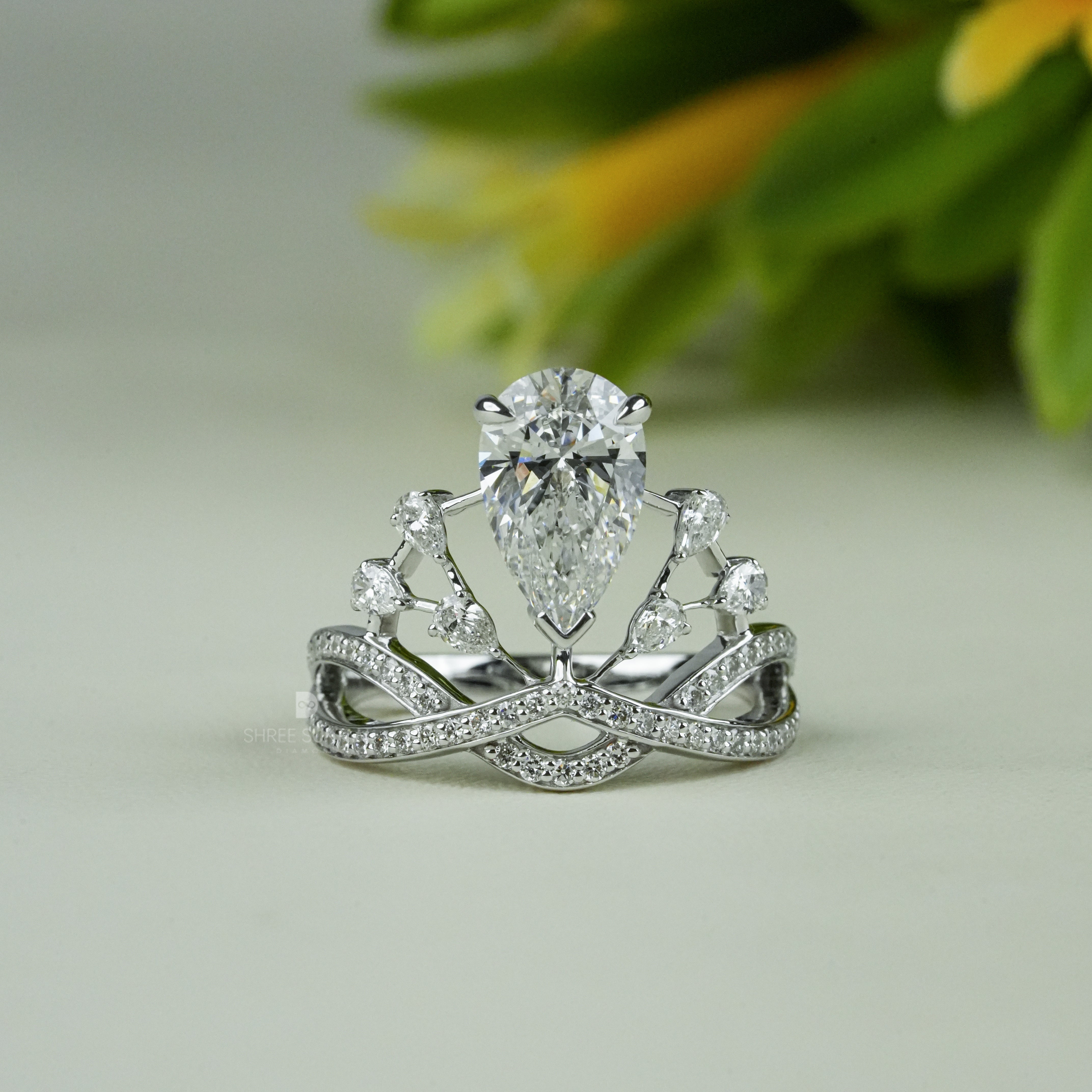 Elegant white gold tiara-inspired engagement ring featuring a stunning pear-shaped center diamond. The crown-style design is accentuated with smaller round diamonds on a double band adorned with pavé-set stones. Perfect for a bride who desires a regal and unique bridal look, this handmade piece combines royalty-inspired elegance with modern sophistication. Ideal as a proposal, promise, or anniversary ring.